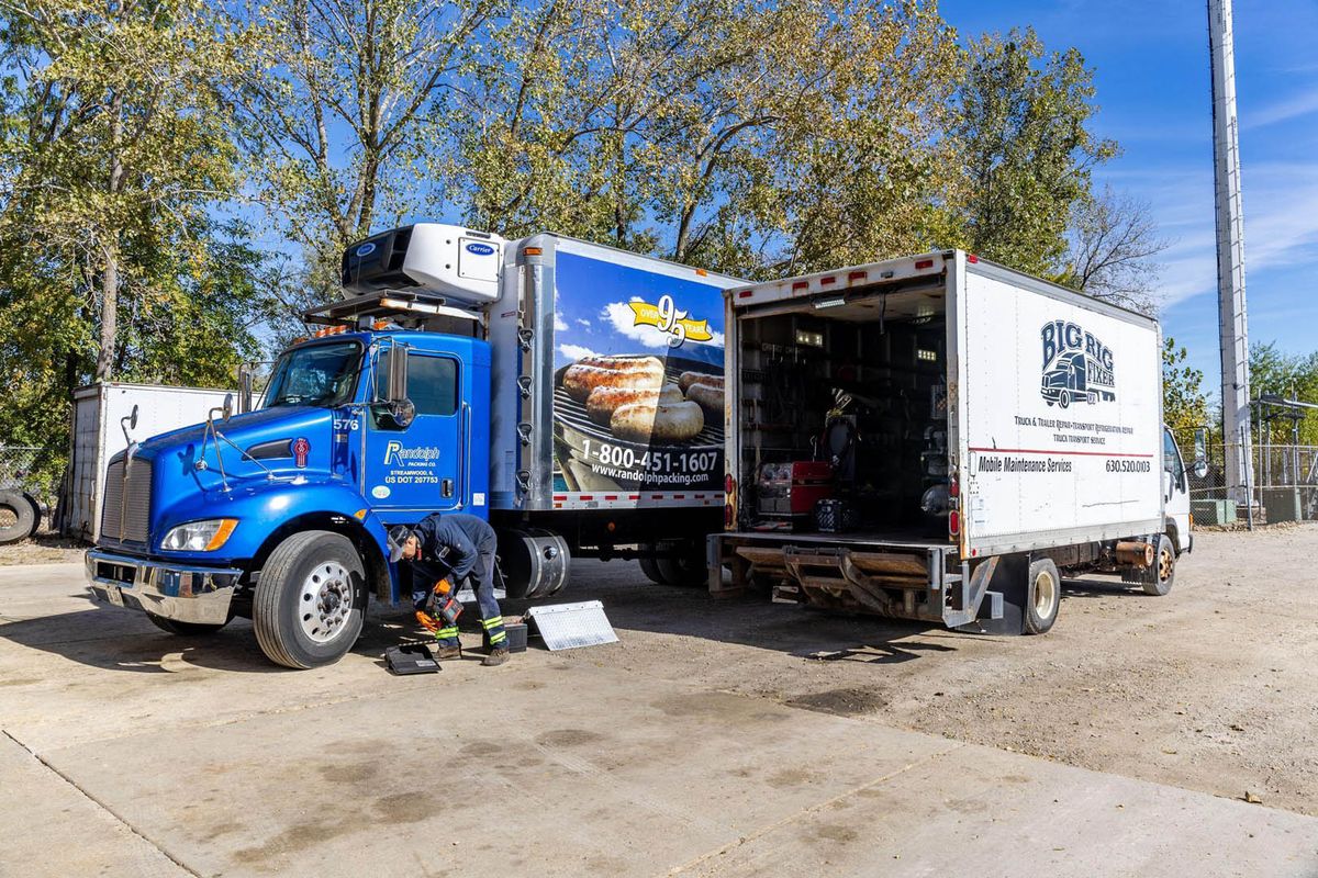 Technician servicing a refrigerated box truck in the Big Rig Fixer yard
