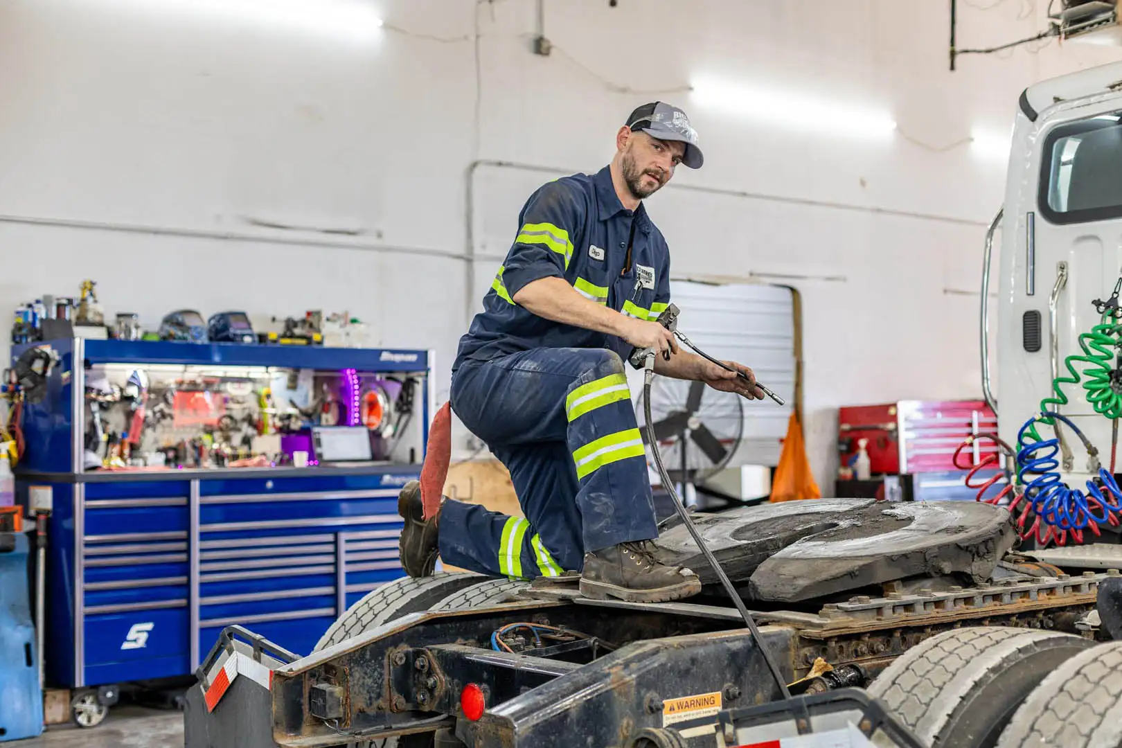 Big Rig Fixer technician in uniform greasing a tractor's fifth wheel in the shop